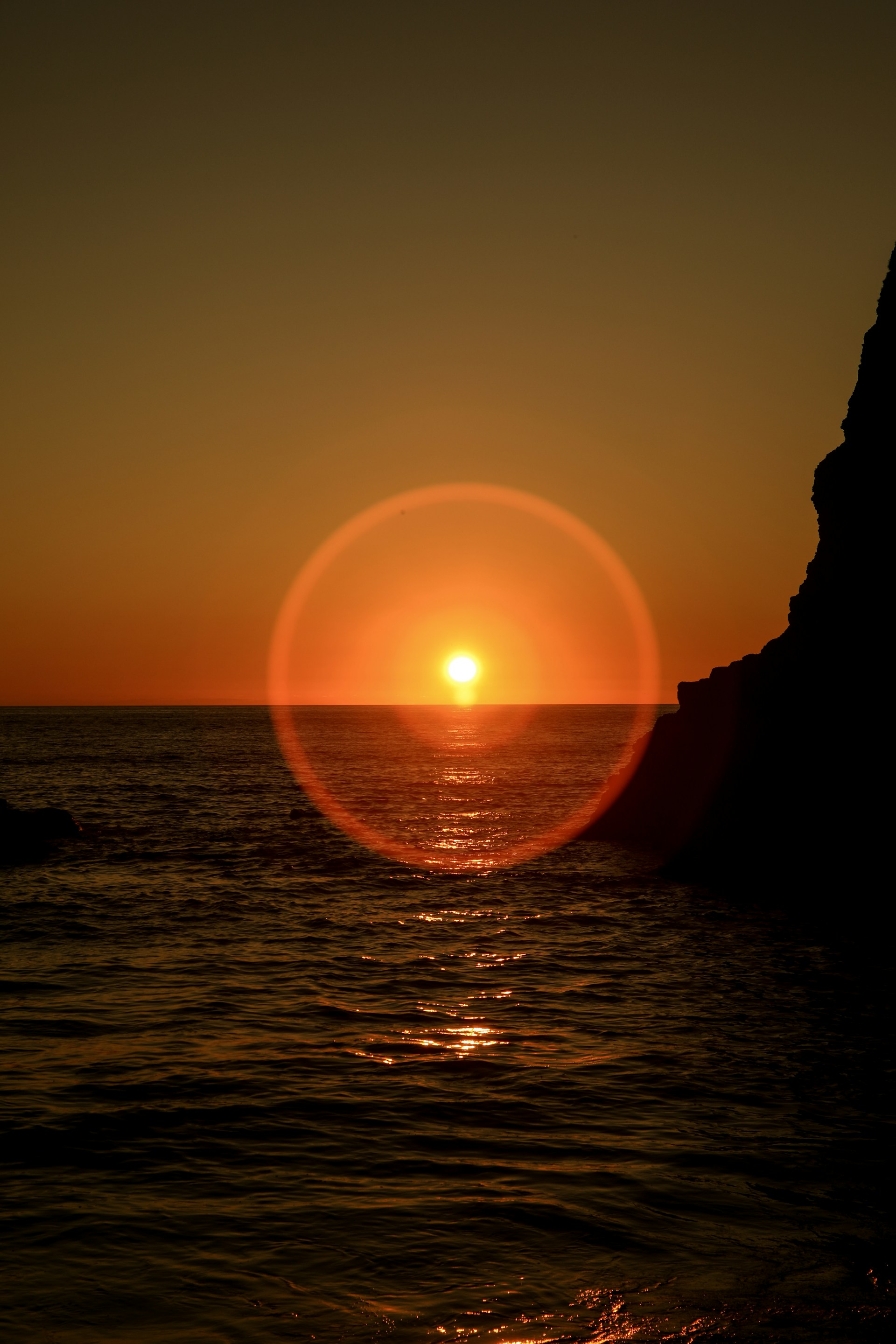 The sun over water with a ring of light around it.